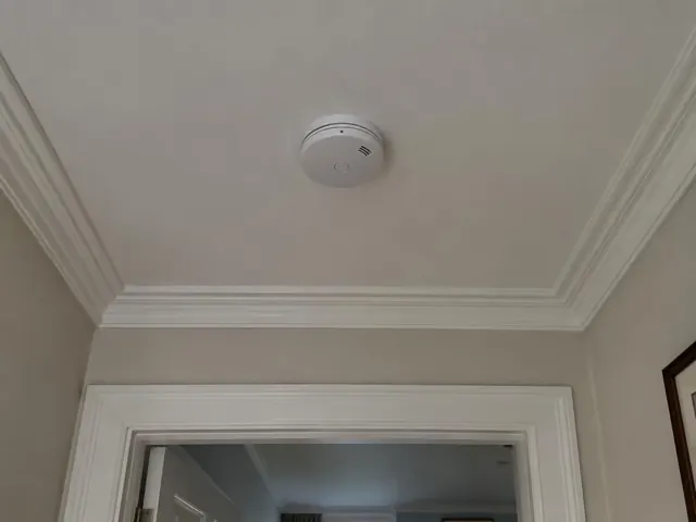 Smoke alarm on a plaster ceiling above a doorway in a heritage-style home in Stanmore