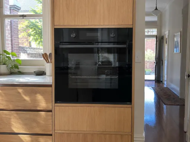 Built-in black wall oven set in light timber cabinetry beside a hallway in Camperdown